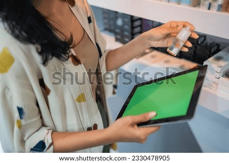 female shopkeeper holding the digital tablet with green screen while checking the liquid at the shelf