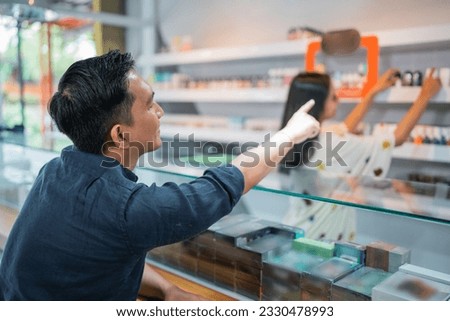 male customer pointing on the liquid arranged at the store shelf to guiding the seller