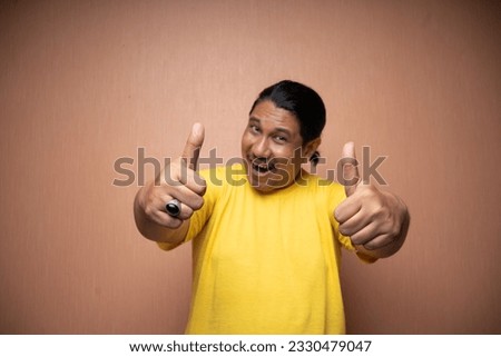 old asian man wearing yellow tshirt with thumbs up gesture showing agreement of something in plain background isolated