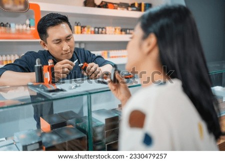 female customer vaping inside the vape store while the male shopkeeper changing the vape cotton in front of her