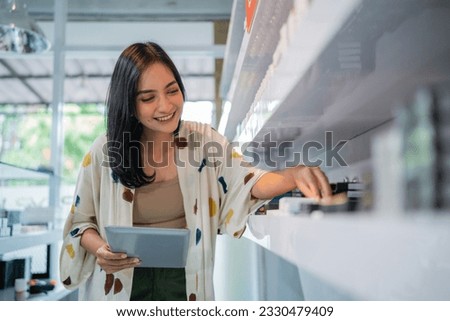 asian shopkeeper smiling while arranging the vape mods stock with the digital tablet at her hand