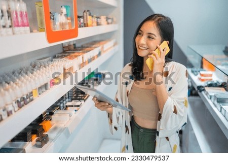female vape seller calling on phone while checking the liquid stock using the digital tablet