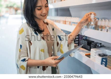 beautiful shopkeeper looking at the digital tablet while checking the liquid stock at the shelf