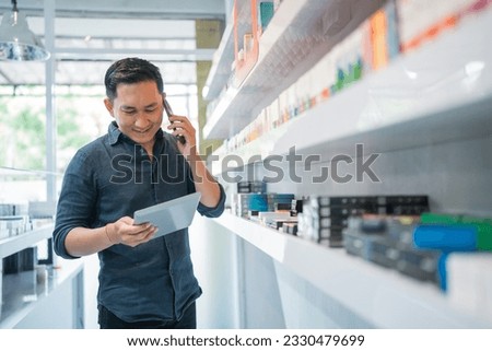 male shopkeeper looking at the digital tablet checking the liquid stock while calling on phone
