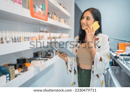 female shopkeeper checking the liquid stock using the digital tablet while calling on phone