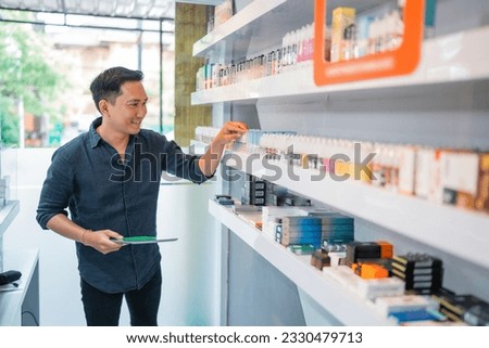 male shopkeeper holding the digital tablet while observing the liquid stock at the shelf