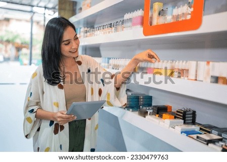 asian shopkeeper arranging the liquid stock at the shelf with the digital tablet at her hand