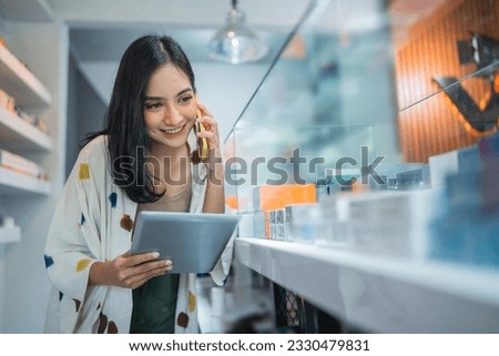 female shopkeeper calling on phone while checking the vape mods stock inside the display table using the digital tablet