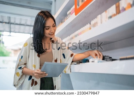 female seller holding the digital tablet while arranging the vape mods at the shelf