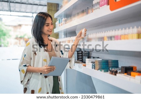 female shopkeeper smiling while checking the liquid stock at the vape store using the digital tablet