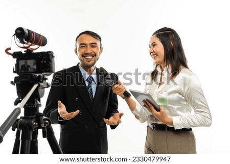 an adult men in black suit talking to the camera while interviewed by a beautiful female journalist using a microphone