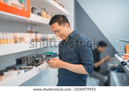 male vape seller looking at his phone while standing beside the store shelf