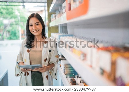 smiling vape seller standing beside the store shelf while holding the digital tablet