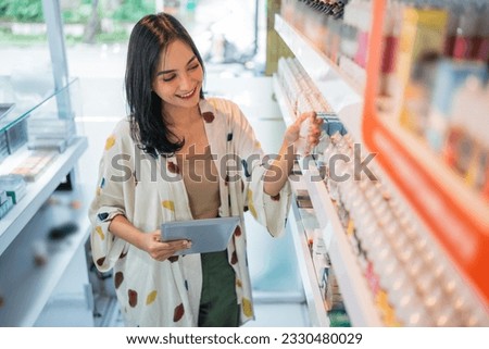beautiful shopkeeper checking the liquid stock at the shelf using the digital table