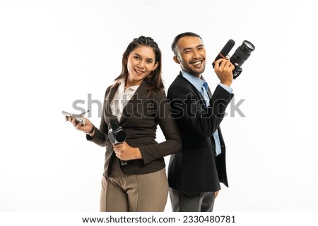 a male journalist standing with a camera at his hand beside a female journalist in brown blazer