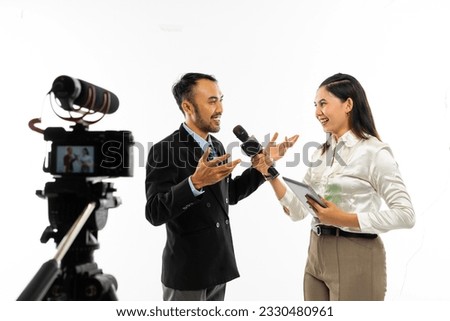 a beautiful female journalist in white blouse interviewing an adult men in black suit using a microphone and recorded by one set of camera