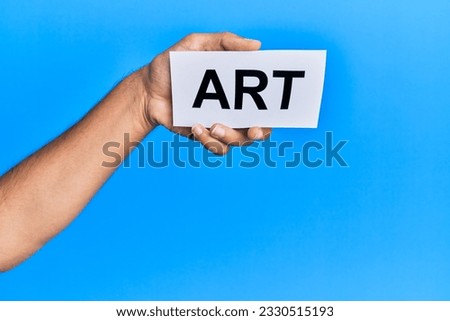 Hand of caucasian man holding paper with art word over isolated blue background