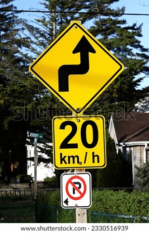 Traffic sign. Bend in road. Speed limit 20. No parking. Yellow and black. Red and white. Wooden sign post. Residential area. Arrow.