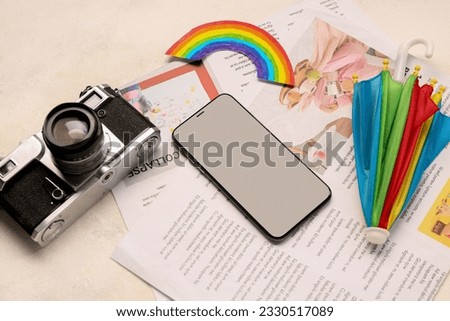 Mobile phone with photo camera, rainbow, umbrella and newspapers on grunge background. Weather forecast concept