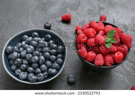 Bowls with fresh raspberry and blueberry on black background, closeup