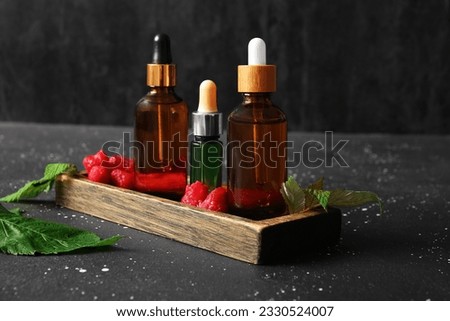 Wooden tray with bottles of cosmetic raspberry oil on black background