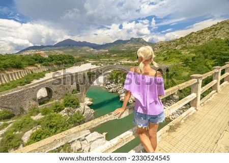 Woman visiting Mesi Bridge, also known as Ura e Mesit, is an Ottoman-era bridge located in the village of Mes, Albania. Largest bridge in Albania from Ottoman period, constructed in 18th century. Royalty-Free Stock Photo #2330524545