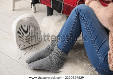 Woman warming legs in socks near radiator at home, closeup Royalty-Free Stock Photo #2330529629