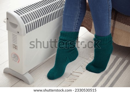 Woman in socks warming near radiator at home, closeup Royalty-Free Stock Photo #2330530515