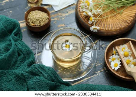 Cup of hot tea and bowl with dried chamomile on black wooden background Royalty-Free Stock Photo #2330534411