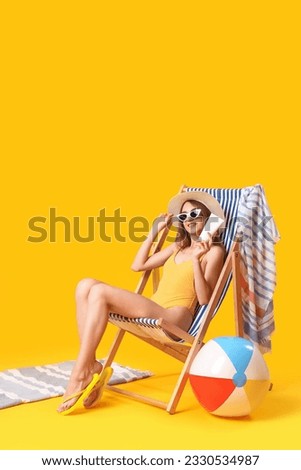 Young woman with sunscreen cream sitting in deck chair on yellow background