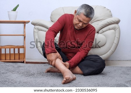 Senior man sitting on floor have cramps in his calves, massage the calf by hands.