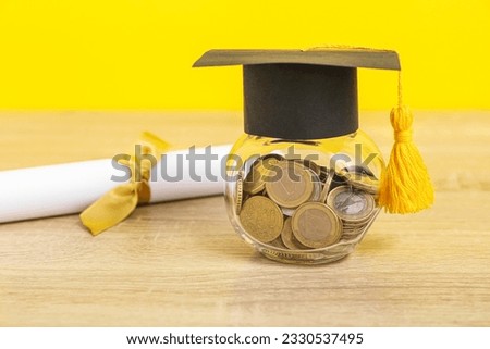 Jar with coins, graduation cap and diploma on wooden table against yellow background. Student loan concept