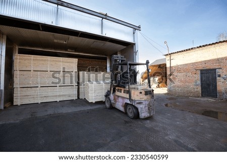 A diesel forklift loads freshly sawn pine logs, girders, bars, beams, bars, boards into a drying chamber. Industrial technology of wood production. Royalty-Free Stock Photo #2330540599