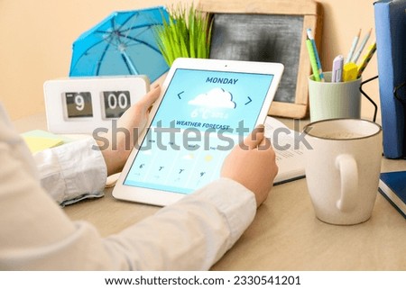 Woman with tablet computer checking weather forecast at table, closeup Royalty-Free Stock Photo #2330541201