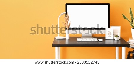 Stylish workplace with modern computer, lamp and photo frames near orange wall. Banner for design