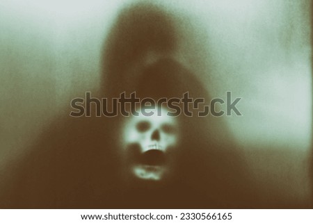 Mysterious man holding a skull in his hand standing behind frosted glass looking mysterious and scary looking like a sorcerer.haunting concept.halloween concept.