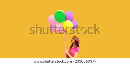 Summer colorful image of happy smiling young woman looking up at multicolor balloons on orange background