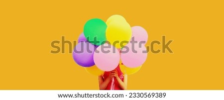 Woman celebrating having fun covering her head holding bunch of colorful balloons on studio background