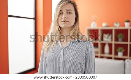 Young blonde woman standing with serious expression at home