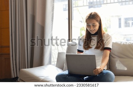Young woman sitting on sofa in living room at home using laptop to research internet learning.