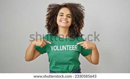 Young beautiful hispanic woman pointing to volunteer uniform smiling over isolated white background Royalty-Free Stock Photo #2330585643