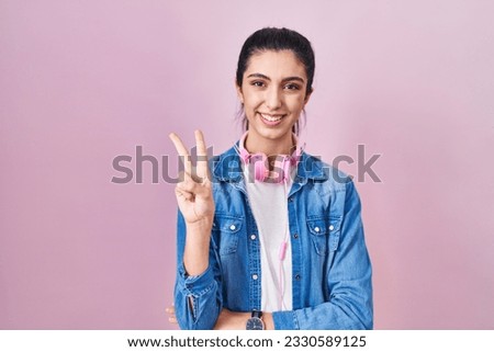 Young beautiful woman standing over pink background showing and pointing up with fingers number two while smiling confident and happy. 
