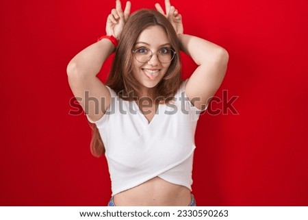 Young caucasian woman standing over red background posing funny and crazy with fingers on head as bunny ears, smiling cheerful 
