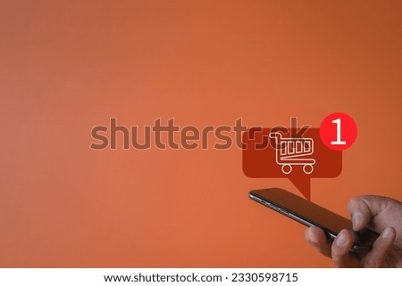 Shopping Online,Digital Marketing,E-commerce,Home delivery concept.,Hand holding smartphone with shopping cart and Notification icon over orange background with copyspace perfect for business idea.