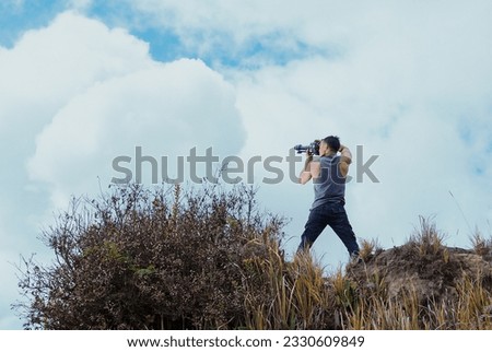 Indonesian male photographer wearing a singlet on a hill with clouds and sky in the background.
SHOTLISTtravel.