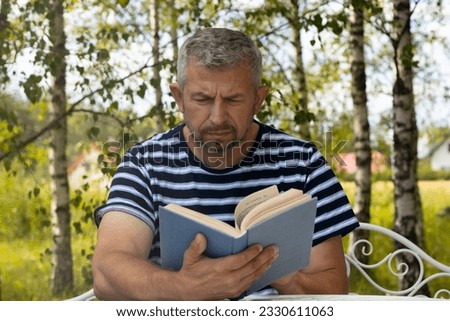 A man is reading a book outside at a table. The man is resting. Soft selective focus. Royalty-Free Stock Photo #2330611063
