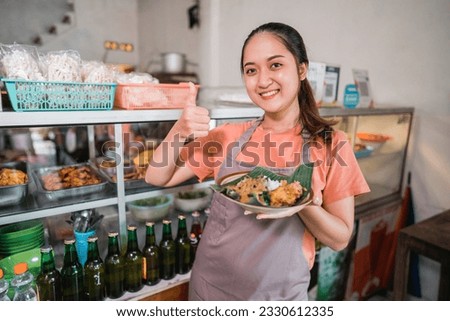 beautiful Asian girl shows thumbs up carrying a plate of pecel food in a food stall Royalty-Free Stock Photo #2330612335