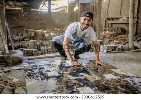 Smiling stonemason squats while washing large squares of stone in the workshop Royalty-Free Stock Photo #2330612529