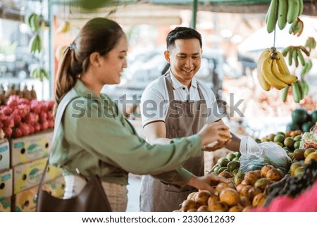 male seller in apron helping the customer preparing her fruits Royalty-Free Stock Photo #2330612639