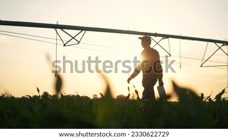 agriculture irrigation. silhouette farmer with a tablet walks through field with corn and a plant for irrigating the field with water. irrigation business agriculture concept. irrigation corn Royalty-Free Stock Photo #2330622729